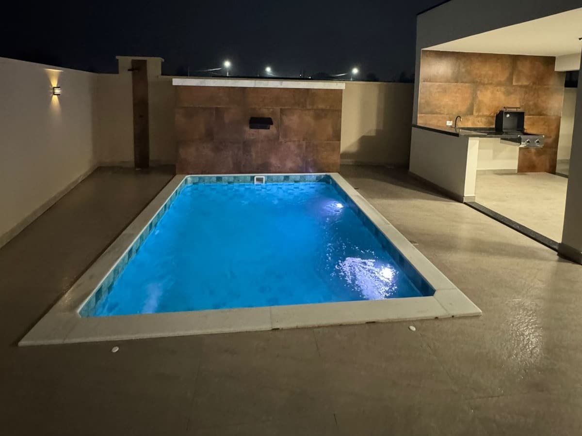 Piscina da Casa 1 com iluminação e cascata, vista de frente, à noite.