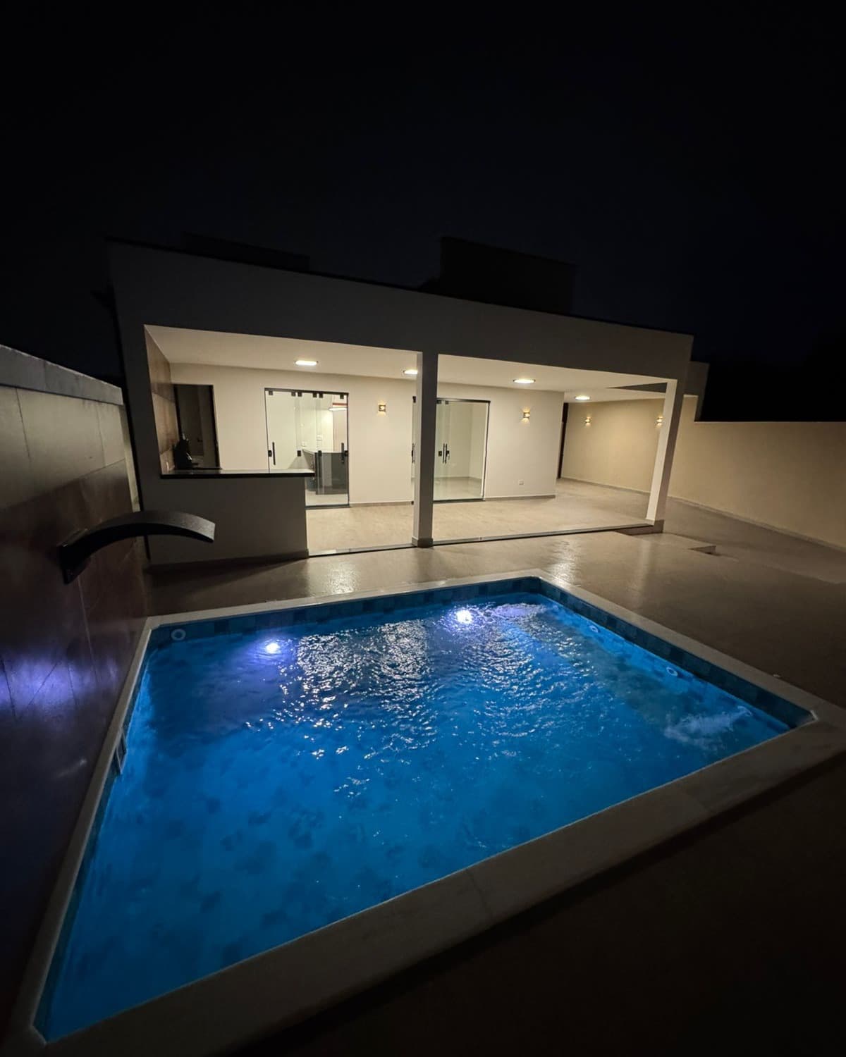 Piscina iluminada da Casa 1 à noite, com a área gourmet e a varanda ao fundo.